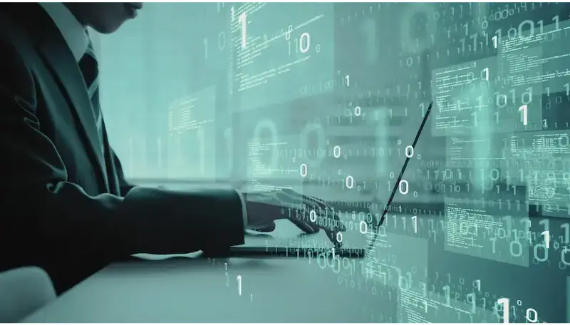 Person in a suit typing on a laptop amidst a digital backdrop of binary code and abstract data.